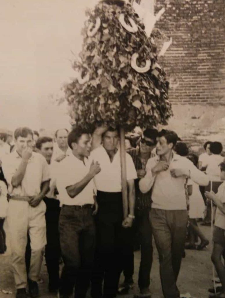 Fotografía antigua en blanco y negro de varios mozos llevando el ramo de la Malena, un gran armazón de ramas con roscas de pan, entre la gente
